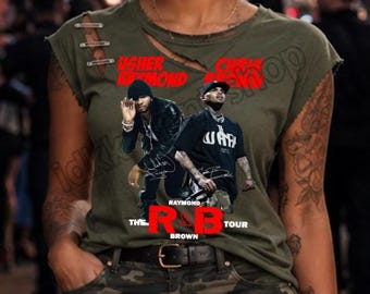 May include: An olive green short-sleeve t-shirt with distressed shoulder detailing and a graphic print featuring Usher and Chris Brown with the text Usher Raymond, Chris Brown, and The R&B Tour in red and white lettering, paired with camouflage pants.