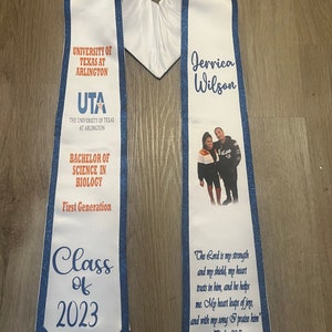 May include: White graduation stole with blue trim and glitter. The stole features the University of Texas at Arlington logo, the text "Bachelor of Science in Biology", "First Generation", "Class of 2023", and a photo of a person with the name "Jerrica Wilson". The stole also includes the text "The Lord is my strength and my shield, my heart trusts in him, and he helps me. My heart leaps of joy, and with my song I praise him." Psalm 28:7