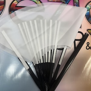 May include: A white fabric fan with black and white striped sticks. The fan is folded and has a white background with black stripes.