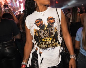 May include: A white sleeveless t-shirt featuring a graphic print of Usher and Chris Brown with the text R&B TOUR USHER & CHRIS BROWN SUMMER 2025. The shirt has side cutouts with tied fabric strips and is paired with black leather pants.