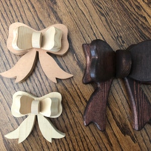 May include: Three wooden bow tie shapes, two are natural wood and one is stained a dark brown.