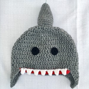 May include: Gray crocheted shark hat with white and red teeth. The hat has black felt eyes.