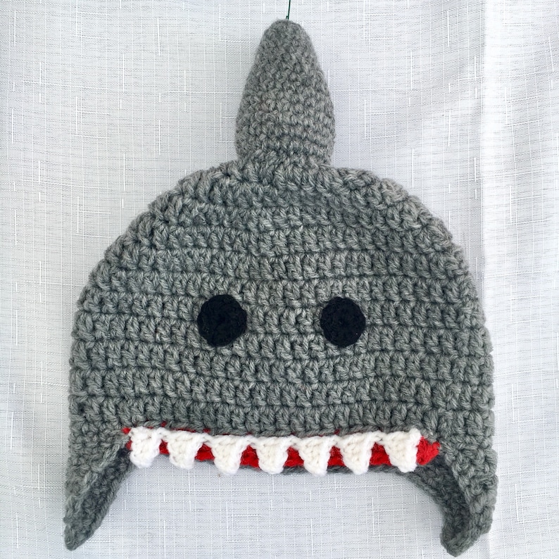 May include: Gray crocheted shark hat with white and red teeth. The hat has black felt eyes.