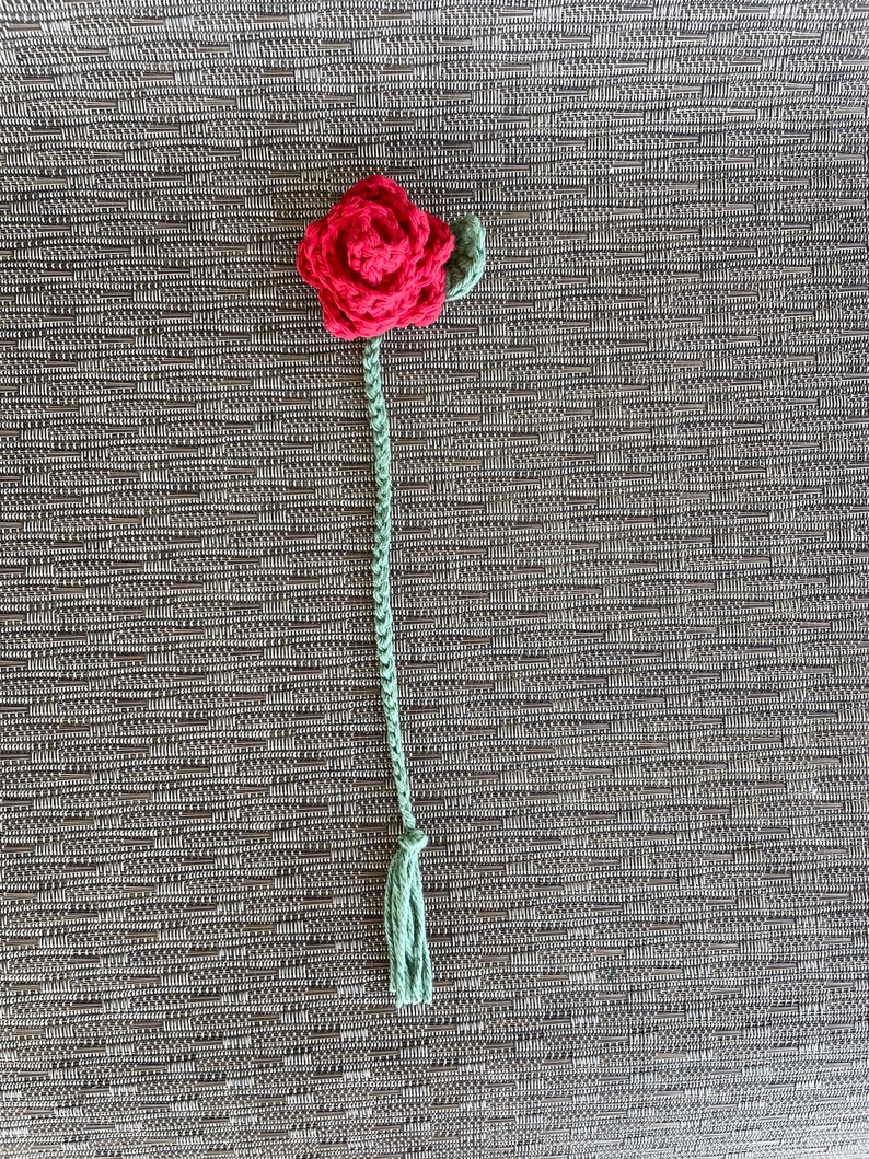 以下が含まれることがあります： 緑の葉と茎が付いた赤い毛糸のバラ。茎の先には緑色の房がついています。