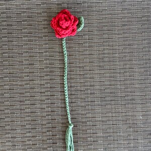以下が含まれることがあります： 緑色の茎と葉が付いた、赤い毛糸で編まれたバラ。バラの茎の先には房がついている。