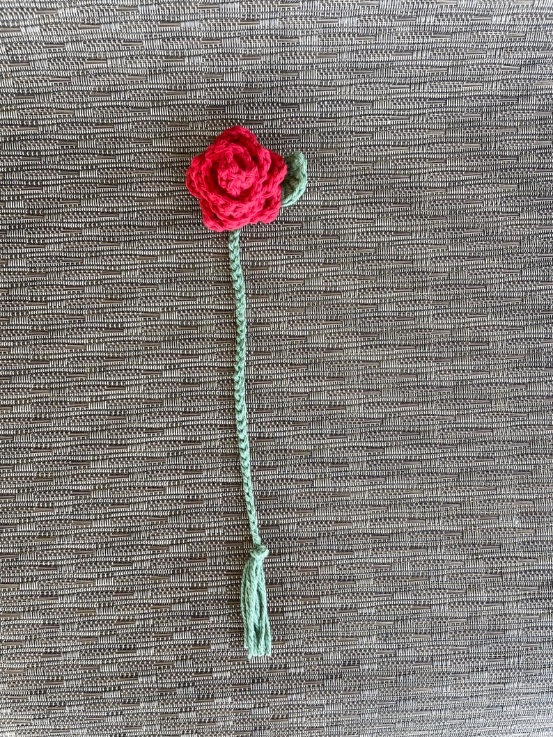 以下が含まれることがあります： 緑色の茎と葉が付いた、赤い毛糸で編まれたバラ。バラの茎の先には房がついている。
