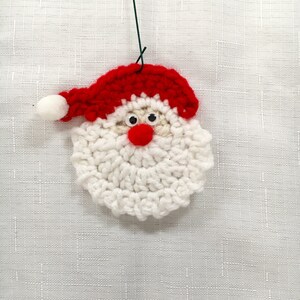 Peut inclure: Une d&eacute;coration de No&euml;l en crochet repr&eacute;sentant le P&egrave;re No&euml;l avec une barbe blanche, un chapeau rouge et des yeux globuleux.