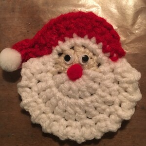 Peut inclure: Une d&eacute;coration de No&euml;l en crochet repr&eacute;sentant le P&egrave;re No&euml;l avec une barbe blanche, un chapeau rouge et des yeux globuleux.