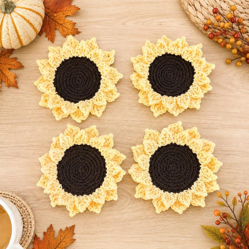 May include: Four round crochet coasters designed to resemble sunflowers, each featuring a dark brown circular center surrounded by light yellow petals. The coasters are arranged in a square formation, showcasing the detailed yarn texture and stitching.
