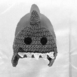 May include: A gray crocheted shark hat with white teeth and black eyes.