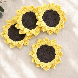 May include: Three circular crochet coasters designed to resemble sunflowers. Each coaster features a dark brown center with a textured, spiraled stitch pattern, surrounded by a border of bright yellow petals crafted with a delicate crochet technique.