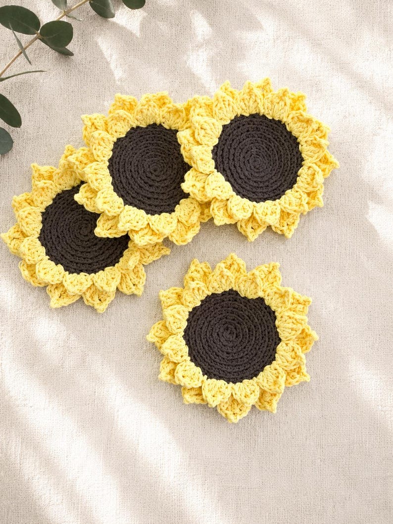 May include: Three circular crochet coasters designed to resemble sunflowers. Each coaster features a dark brown center with a textured, spiraled stitch pattern, surrounded by a border of bright yellow petals crafted with a delicate crochet technique.
