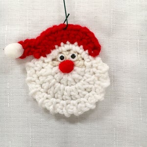 Peut inclure: Une d&eacute;coration de No&euml;l en crochet repr&eacute;sentant un P&egrave;re No&euml;l avec une barbe blanche, un chapeau rouge et des yeux noirs. La d&eacute;coration est suspendue &agrave; un fil de fer vert.