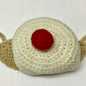 May include: A white crocheted snail hat with a red crocheted flower on top.