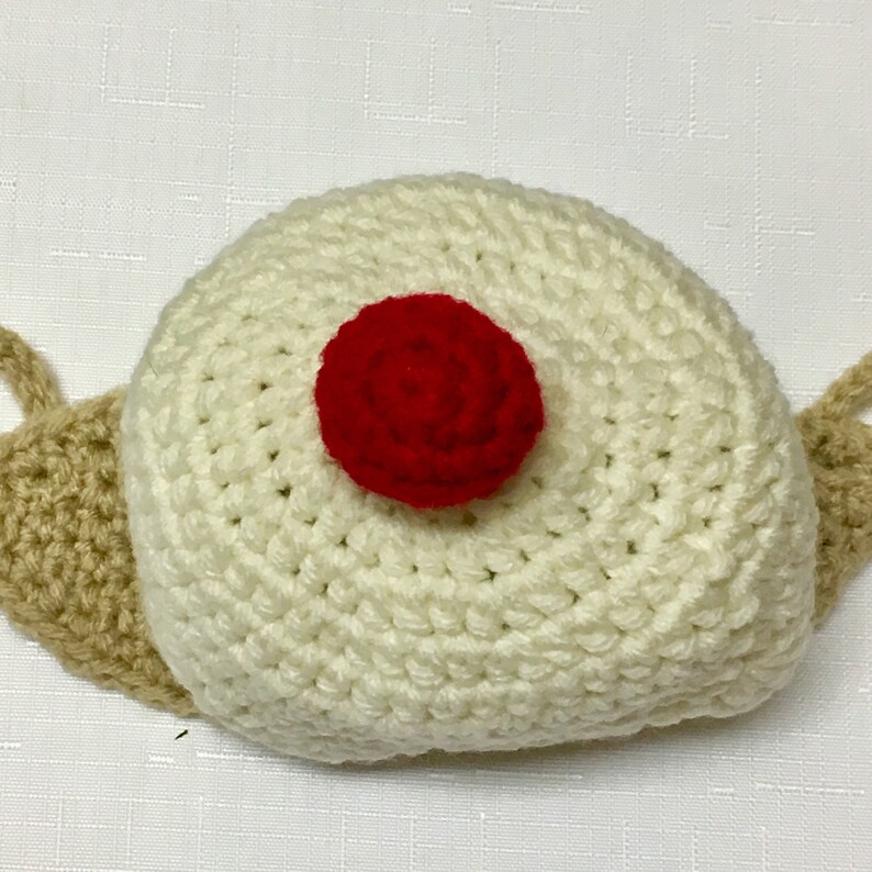 May include: A white crocheted snail hat with a red crocheted flower on top.