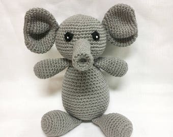 Può includere: Un giocattolo di elefante di uncinetto grigio con occhi neri. L'elefante è seduto con le gambe distese.