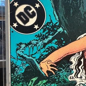 May include: Comic book cover featuring the DC logo in a black circle with white stars. The artwork depicts a scene with a hand reaching out, surrounded by green and blue foliage, and the title "THE".