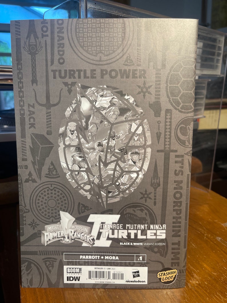 May include: A black and white comic book cover featuring the Teenage Mutant Ninja Turtles and the Mighty Morphin Power Rangers. The cover has the title "Teenage Mutant Ninja Turtles" and "Black & White Variant Edition". The cover also has the text "It's Morphin Time" and "Parrott &bull; Mora #1".