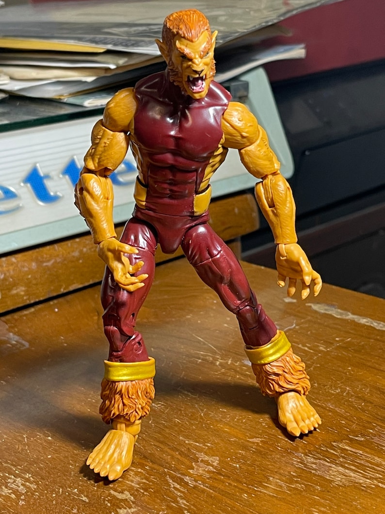 May include: A red and gold action figure of a werewolf with a snarling expression. The figure has a muscular build and is posed in a dynamic stance.