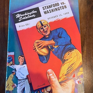 May include: A vintage program for a football game between Stanford and Washington. The cover features a red background with the text "Stanford vs. Washington" and "October 15, 1949". A football player in a blue and yellow uniform is depicted in action, holding the ball. The program is titled "Washington  Sideliner" and priced at 35 cents.