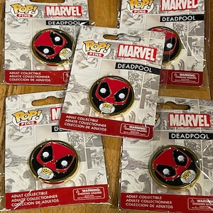 May include: Five collectible Deadpool pins featuring a red and black Deadpool head with a speech bubble that says "Pop! Marvel". The pins are packaged in clear plastic bags with a white background and black text that says "Pop! Pins Marvel Deadpool".