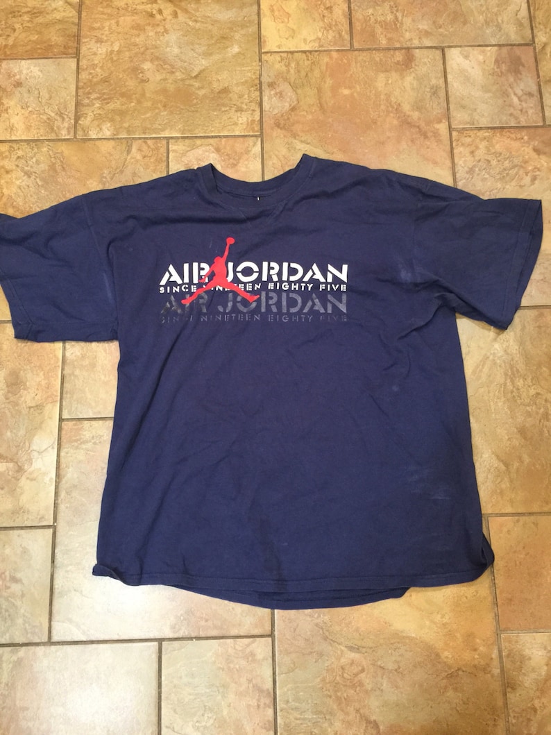 May include: A navy blue t-shirt with a white graphic print of a basketball player with the text "Air Jordan Since Nineteen Eighty Five" repeated twice.