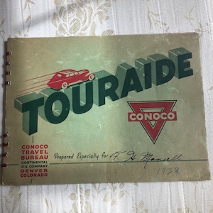 May include: A vintage travel guide booklet with a red car driving up a set of stairs. The cover features the text "Touraide" in green and "Conoco" in red. The booklet is titled "Conoco Travel Bureau Continental Oil Company Denver Colorado" and is signed "Prepared Especially for F. H. Mancell 1939."