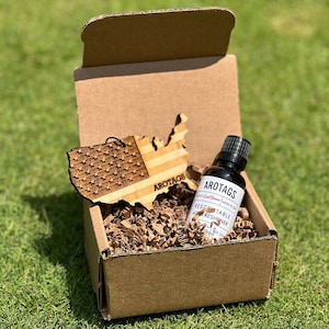 May include: A brown cardboard box containing a wooden American flag cutout and a small bottle of car air freshener. The bottle is labelled "Arotags" and "Rescentable Air Freshener".