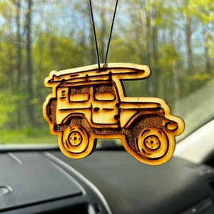 以下が含まれることがあります： サーフボードを載せたヴィンテージオフロード車の形をした木製カーエアフレッシュナー。エアフレッシュナーは、濃い茶色のエッチングが施された明るい茶色の木材で作られています。黒い紐から吊り下げられています。