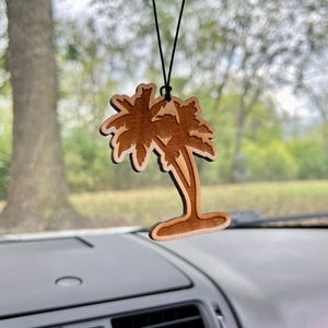 May include: A wooden palm tree car air freshener hanging from a rearview mirror. The palm tree is brown and has a detailed design.