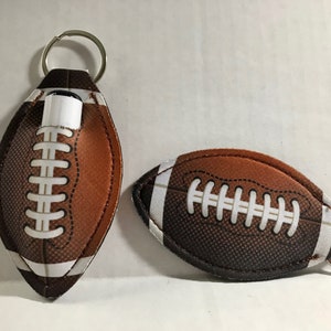 May include: Two brown and white football-shaped keychains. One keychain has a silver ring and a small white tube inside. The other keychain has a silver ring.