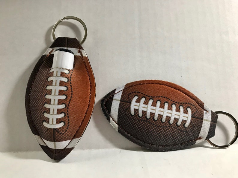 May include: Two brown and white football-shaped keychains. One keychain has a silver ring and a small white tube inside. The other keychain has a silver ring.