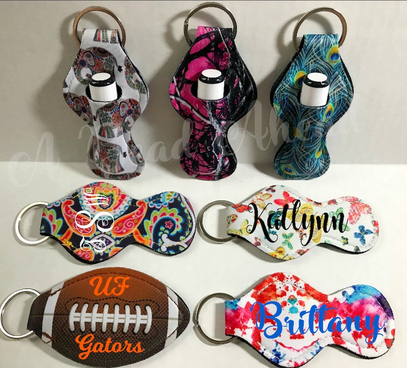 May include: Seven different lip balm holders with keychains. The holders are made of neoprene and have various patterns including paisley, butterflies, camouflage, peacocks, elephants, tie dye, and a football with the words 'UF Gators'.