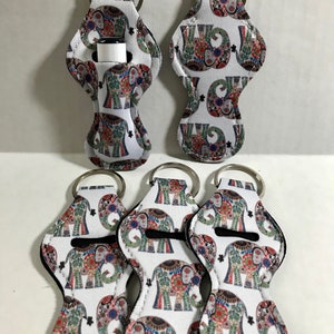 May include: Five white lip balm holders with a colorful elephant print design. Each holder has a silver key ring attached.
