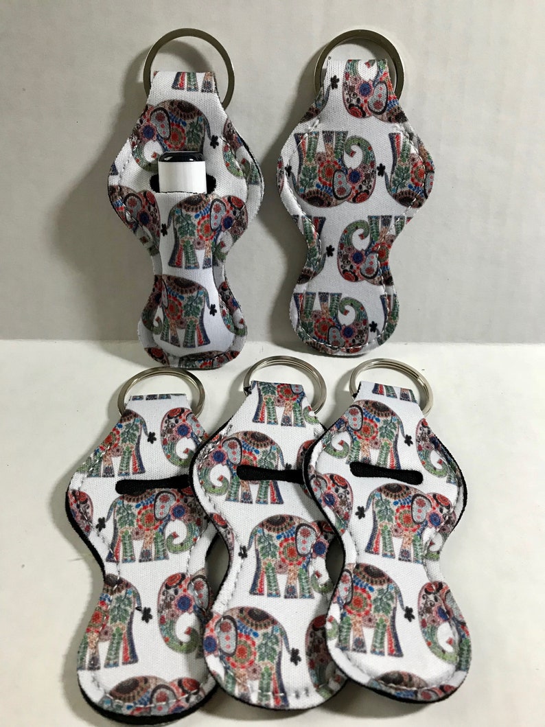 May include: Five white lip balm holders with a colorful elephant print design. Each holder has a silver key ring attached.