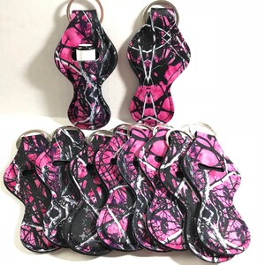 May include: Ten pink and black camo lip balm holders with silver key rings. The holders are made of fabric and have a lip balm tube slot.