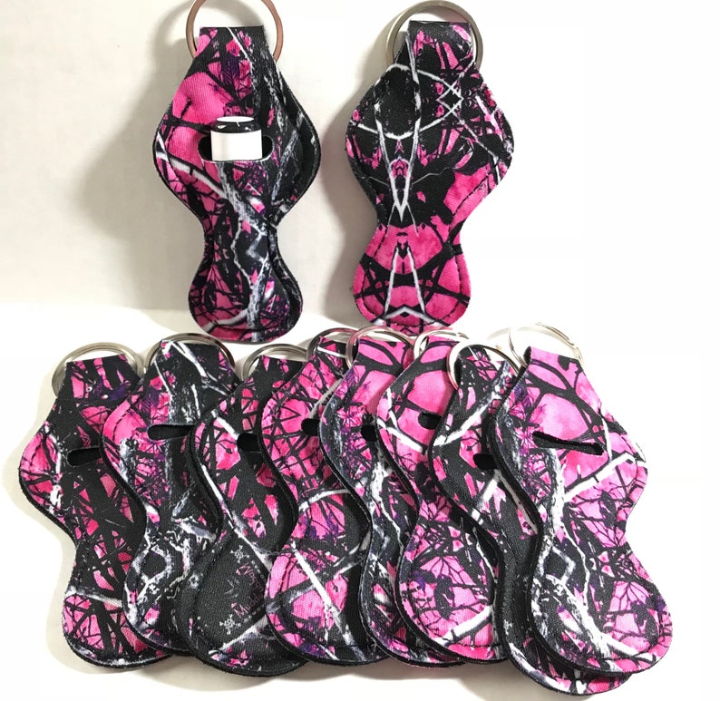 May include: Ten pink and black camo lip balm holders with silver key rings. The holders are made of fabric and have a lip balm tube slot.
