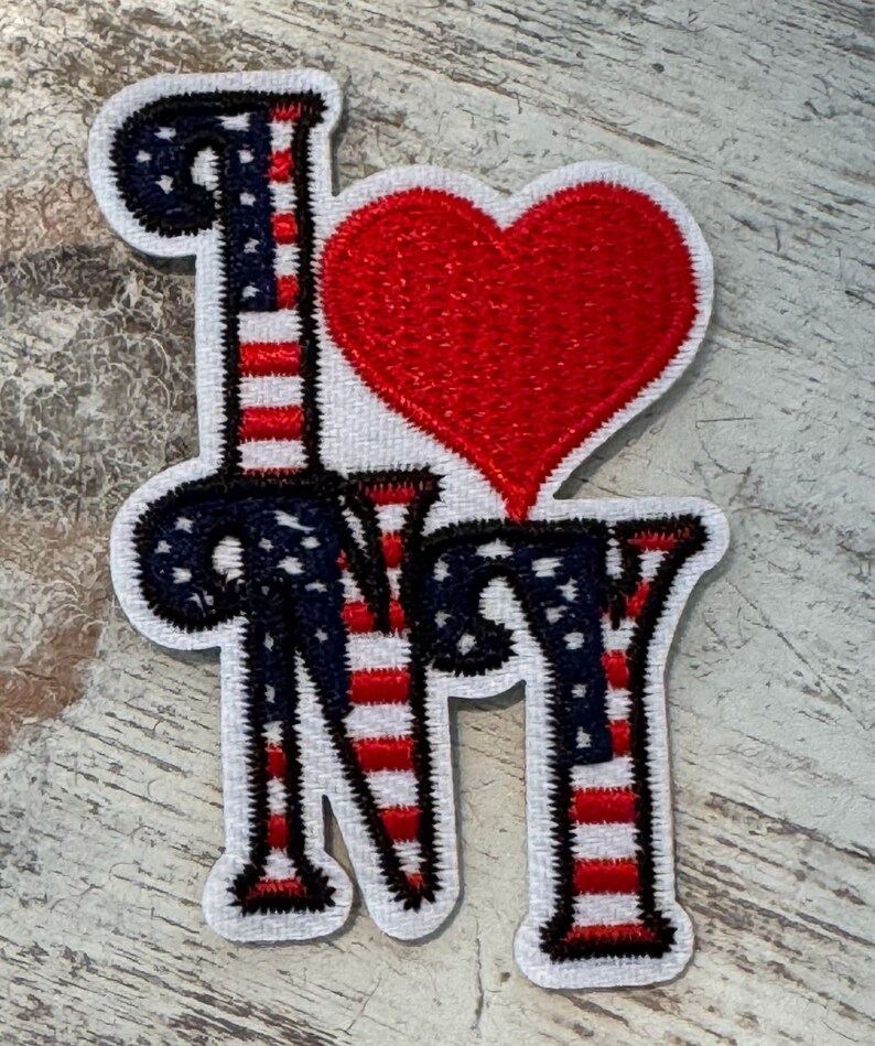 Pu&ograve; includere: Una toppa ricamata con le parole "I Love NY" in un font stilizzato. Le lettere sono contornate di nero e riempite con strisce rosse e bianche, che ricordano la bandiera americana. Un cuore rosso &egrave; posizionato tra la "I" e la "NY".