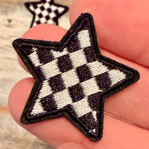 May include: Embroidered star patch with a black and white checkered pattern. The patch has a black border and is held in a hand. The star shape is a classic design element.