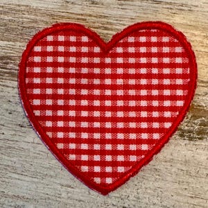 May include: A red and white gingham heart-shaped patch with a stitched border. The patch is a classic design, perfect for adding a touch of charm to clothing, accessories, or crafts. The heart shape is a symbol of love and affection.