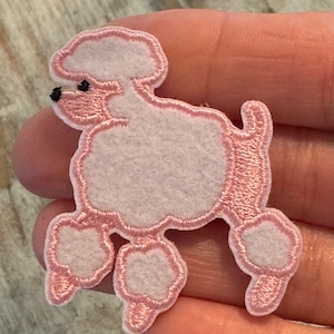 May include: Pink felt poodle applique with black eyes. The poodle is standing on all four legs.
