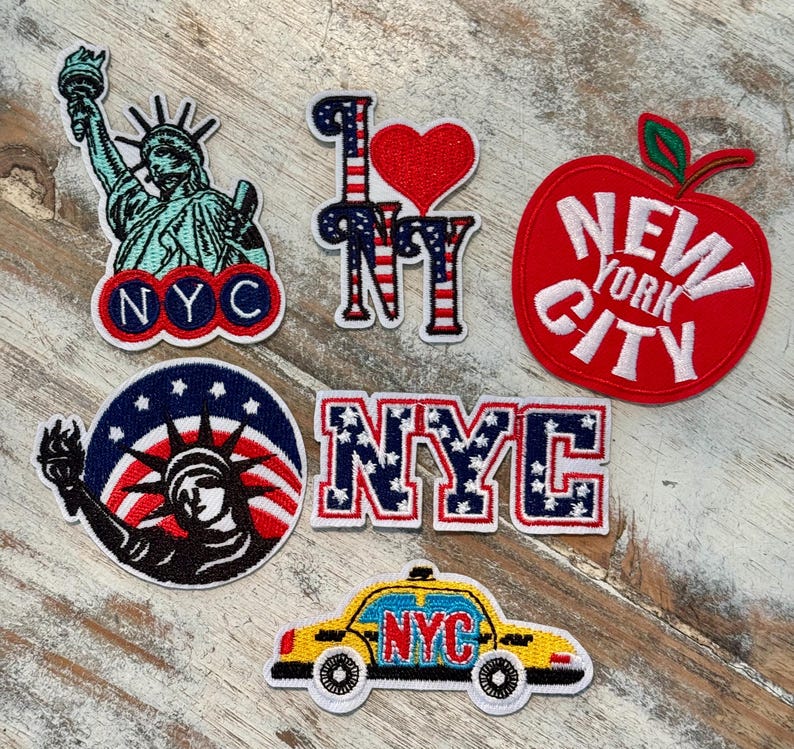 Pu&ograve; includere: Un set di sei toppe da stirare con temi della citt&agrave; di New York. Le toppe includono una mela rossa con il testo "New York City", una Statua della Libert&agrave; con una bandiera americana, un cuore rosso con il testo "I Love NY", un testo "NYC" blu e rosso con stelle, una Statua della Libert&agrave; con una bandiera americana in un cerchio e un taxi giallo con il testo "NYC".