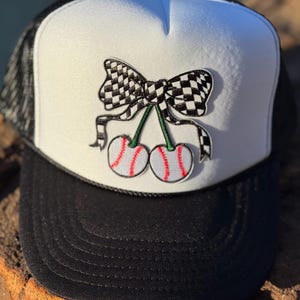 May include: A white and black checkered bow with a cherry design on a black and white trucker hat.