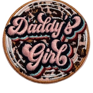 May include: A round, embroidered patch with a leopard print background. The text "Daddy's Girl" is in pink, blue, and black lettering.