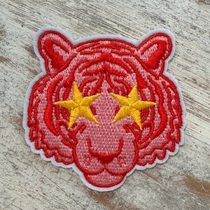 May include: Pink embroidered tiger face patch with yellow star-shaped eyes.