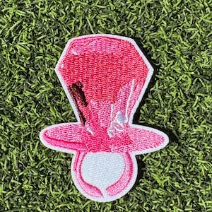 May include: Embroidered pink pacifier patch with a white border. The patch features a pink top hat design with a white bow and a dark brown accent. The pacifier portion is white with a pink outline.