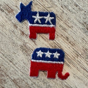 May include: Two felt political party animal patches. A blue donkey with three white stars and a red elephant with three white stars. Both patches have a white stripe and red body.