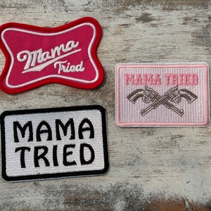 May include: Three pink and white embroidered patches with the text "Mama Tried" in white. The top patch has a red background. The middle patch has a white background and two crossed pistols. The bottom patch has a black background.