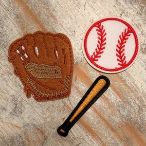 May include: Three baseball-themed patches: a brown baseball glove, a white baseball with red stitching, and a black and gold baseball bat. The patches are likely for decorative purposes, such as for clothing or accessories.