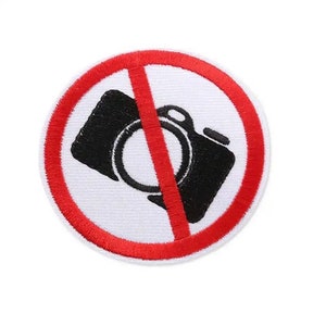 May include: A red circle with a diagonal line through a black camera icon. The sign indicates that photography is prohibited.